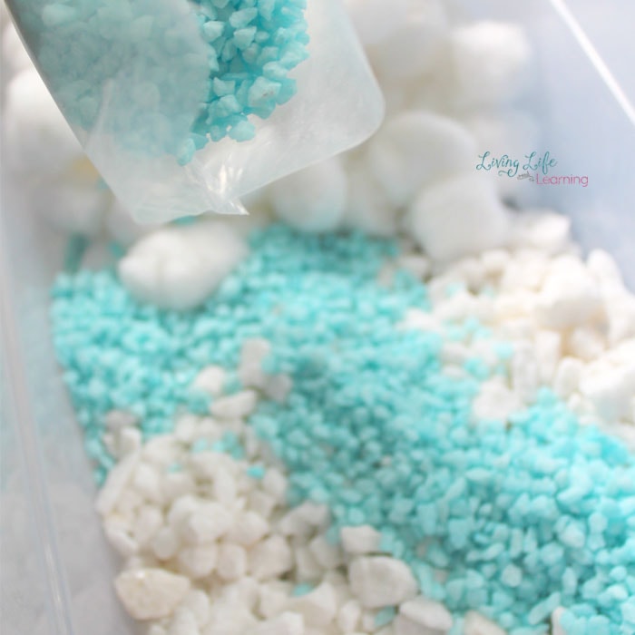 Teal gravel rocks are scattered on top of the white cotton balls and white gravel rocks.