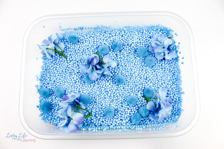 Blue foam beads and blue flowers form the bottom of the easy butterfly sensory bin.