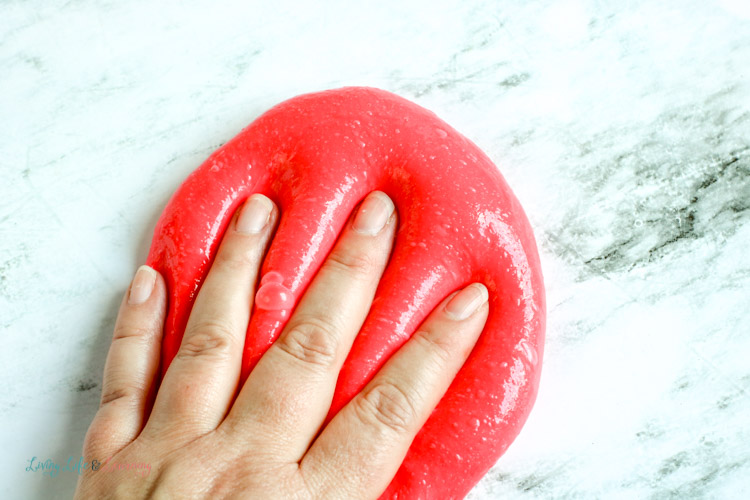 Child's hand pushing on red apple-scented slime
