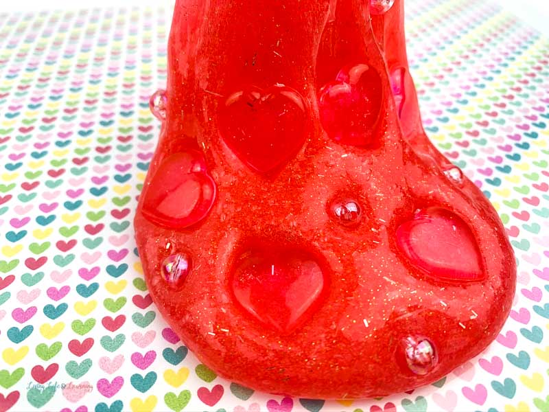 Red glitter slime stretching to show hearts and gems.
