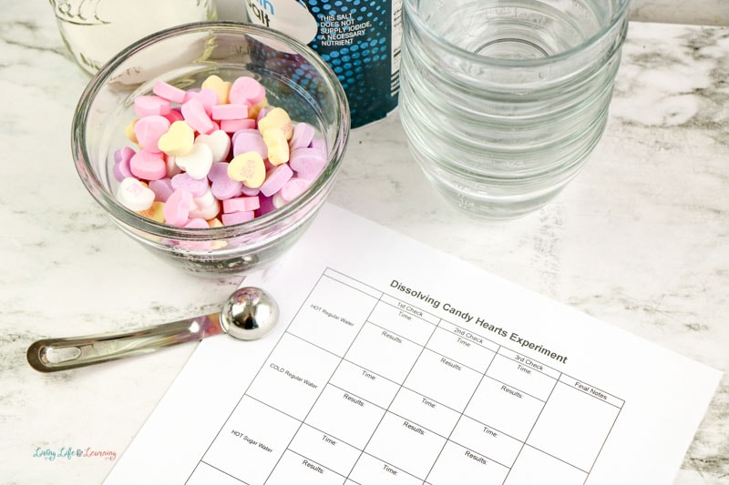 A bowl of candy hearts, stacked glass bowls, and a dissolving candy hearts experiment paper.
