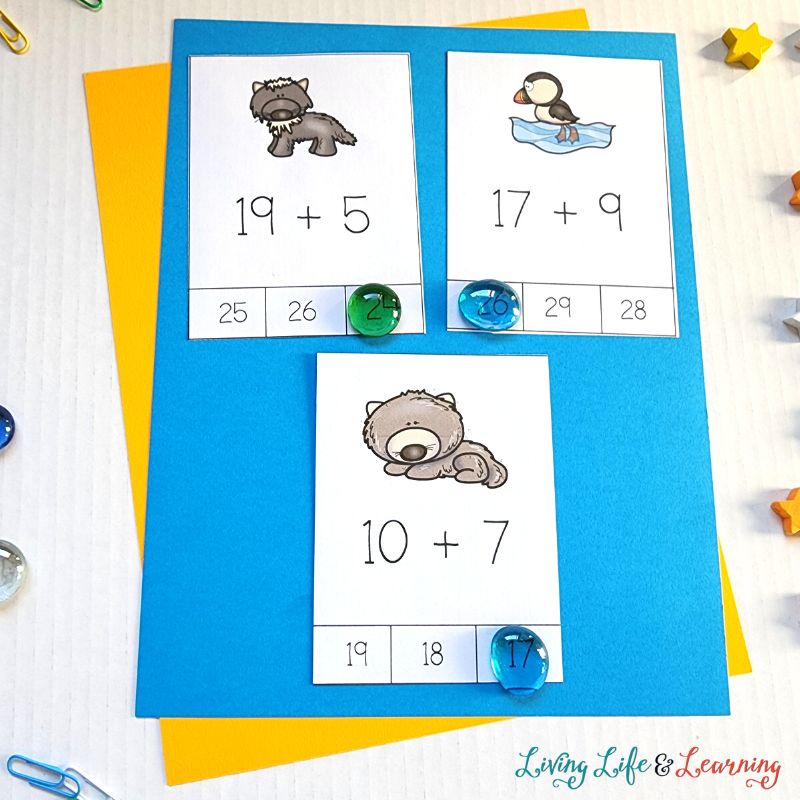 There are three arctic animal addition cards placed on top of the blue-colored paper which is also above a yellow-colored paper.