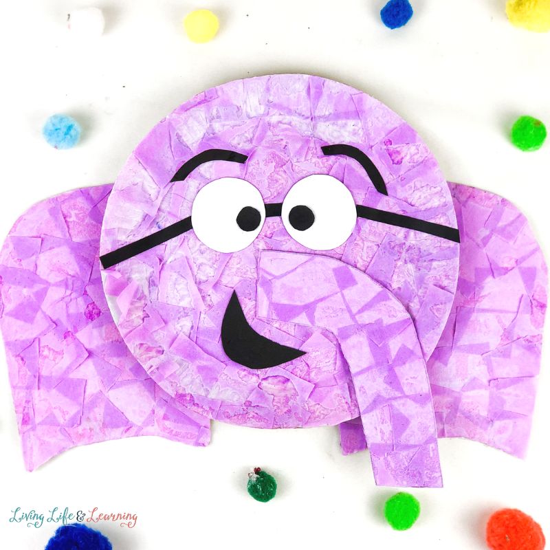 Pink paper plate elephant on white background surrounded by colorful fuzzy balls.