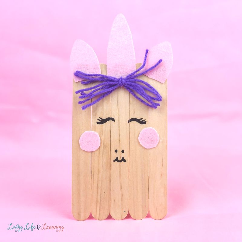Wooden unicorn craft made of popsicles in a pink background.
