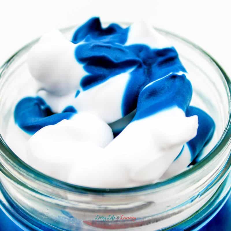 Food coloring is added to the jar with water and shaving cream.
